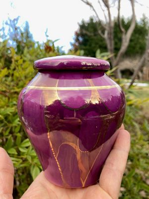 An Ancient Creations ceramic cremation urn in Royal purple with gold luster designs and 22 karat gold band on vessel and lid. Perfect size for pet ashes.