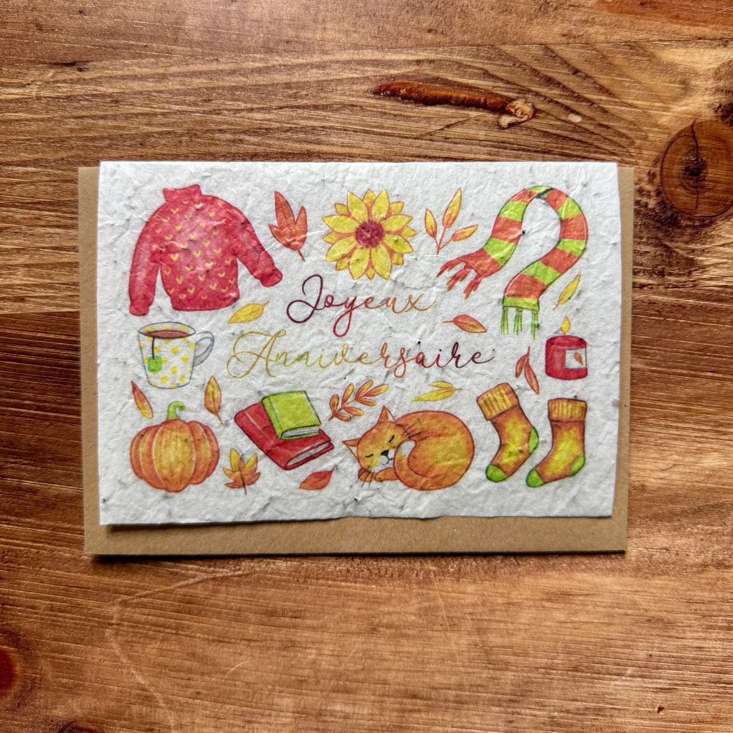 Carte “Joyeux Anniversaire” illustrée d’un pull, d’un chat et de feuilles d’automne aux tons chauds.