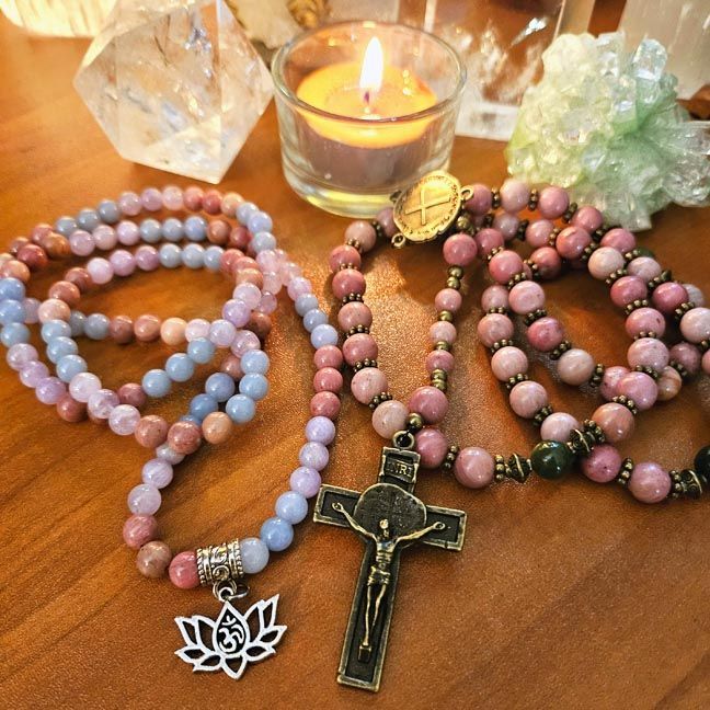 Rosary and prayer beads arranged on a wooden surface with a candle and crystals behind them