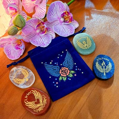 Four engraved Archangel stones arranged around a blue winged pouch with orchids above.