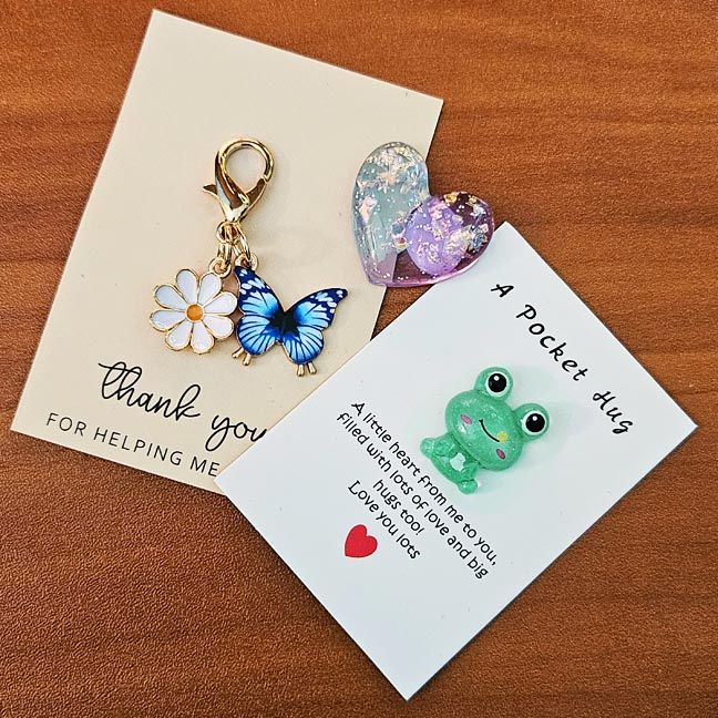 Pocket Charms and Clip‑Ons featuring tiny animals, hearts, and themed designs with inspiring quote cards.