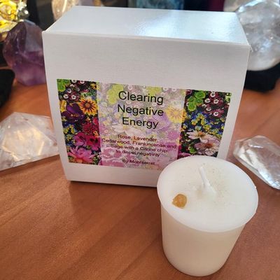 White votive candle with a citrine chip beside a box labeled “Clearing Negative Energy” with a floral design and crystals 