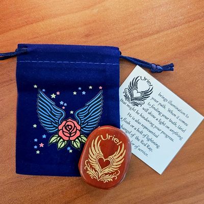 Red jasper Uriel stone beside a blue winged pouch with a rose design and a printed card behind it