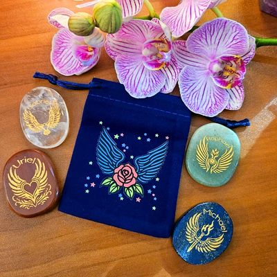 Four engraved gemstone Archangel stones surrounding a blue winged pouch with orchids on top