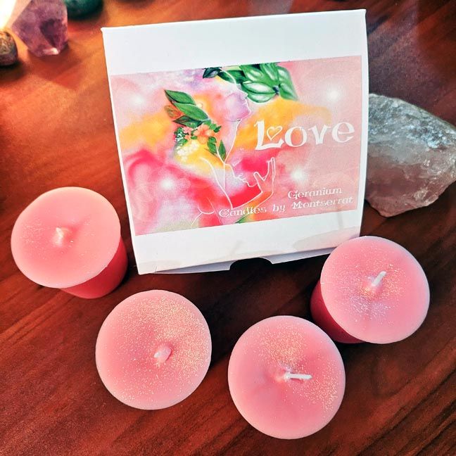 Four pink votive candles beside a box labeled “Love – Geranium – Candles by Montserrat” with colorful abstract floral artwork