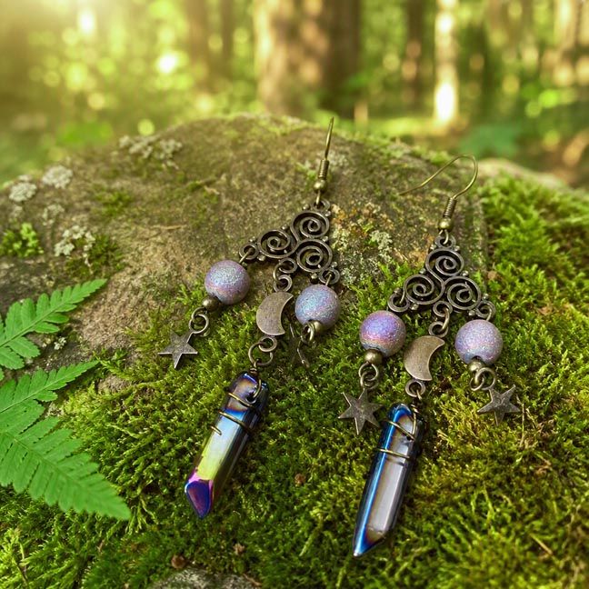 Antique brass Triskele earrings with moon and star charms and titanium quartz crystal, displayed as celestial jewelry.