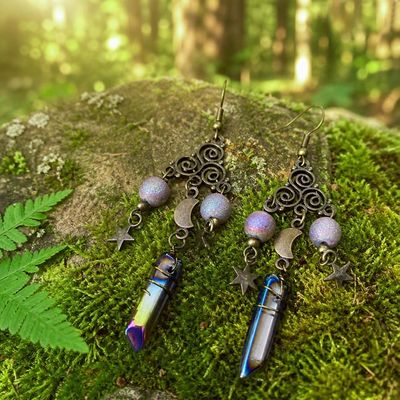 Antique brass Triskele earrings with moon and star charms and titanium quartz crystal, displayed as celestial jewelry.