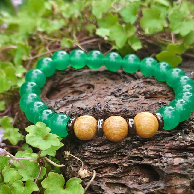 Bracelet with green aventurine beads and three palo santo beads, displayed on brown stone with small green plants
