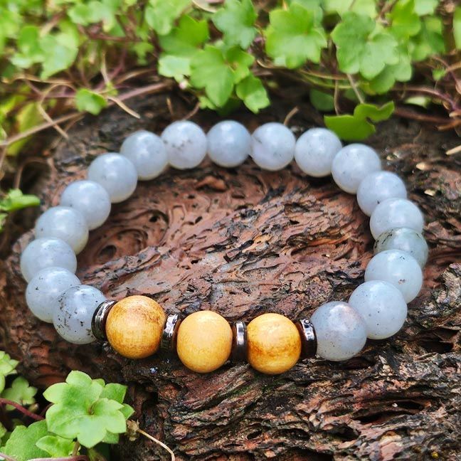 Bracelet with labradorite beads and three larger palo santo beads, displayed on brown stone with small green plants