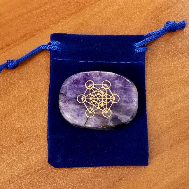 Amethyst palm stone with a gold Metatron engraving placed on a blue velvet pouch on a wooden surface.