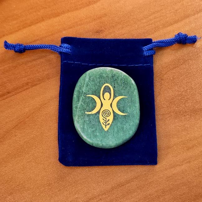 Green Aventurine palm stone with a gold goddess engraving placed on a blue velvet pouch on a wooden surface.