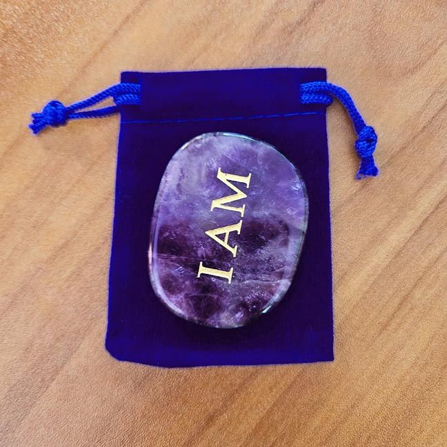 Amethyst palm stone with gold "I AM" engraving placed on a blue velvet pouch on a wooden surface.