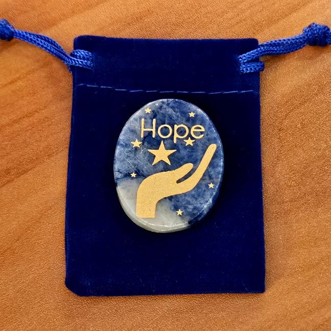 Sodalite palm stone with a gold hand and star engraving placed on a blue velvet pouch on a wooden surface.