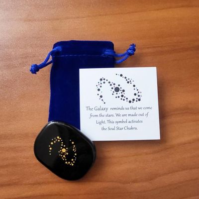 Obsidian palm stone with gold galaxy design shown with a blue velvet pouch and a printed information card.