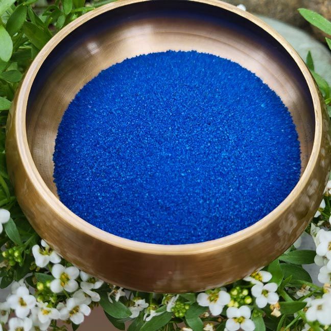 Bronze bowl holding vivid blue sand with white flowers and greenery around it