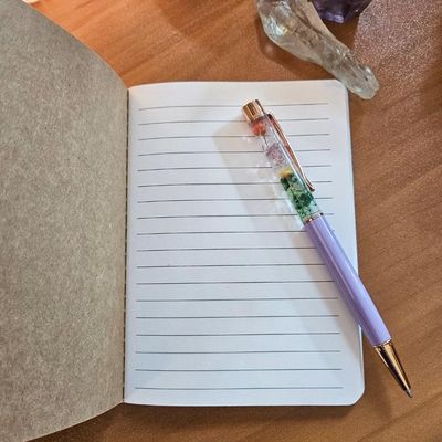 Open stitched notebook with lined pages on a wooden surface, with a pen and two crystals placed nearby
