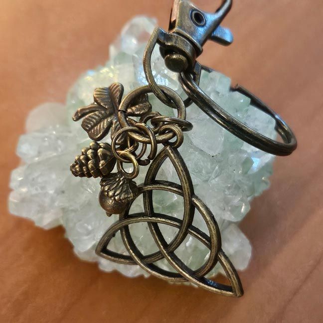 Antique‑bronze triquetra key chain with acorn, clover, and pinecone forest charms.