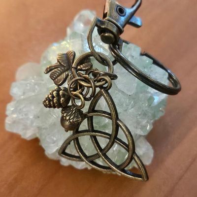 Antique‑bronze triquetra key chain with acorn, clover, and pinecone forest charms.