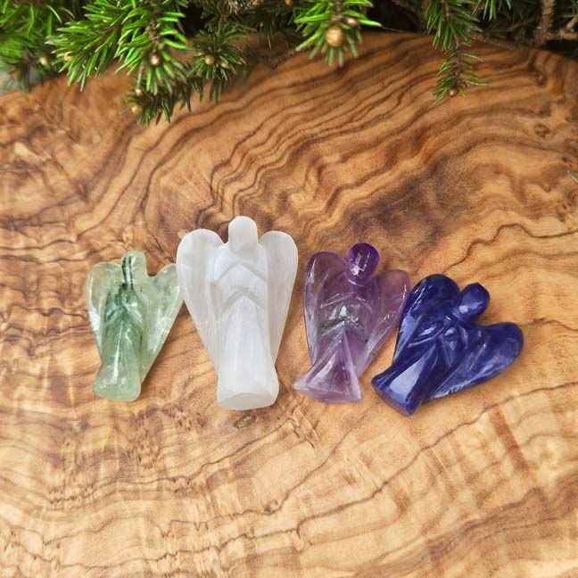 Four small crystal angel figurines in green, white, purple, and dark blue on a wooden surface
