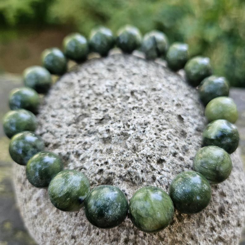 Bracelet made of polished round green Canadian jade beads resting on rough gray stone outdoors