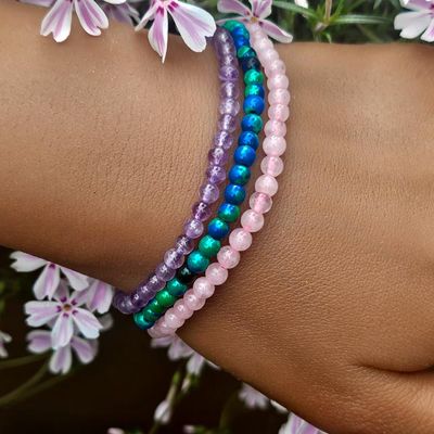 Three thin gemstone bracelets on a wrist, in rose quartz, blue‑green chrysocolla, and amethyst with soft floral background