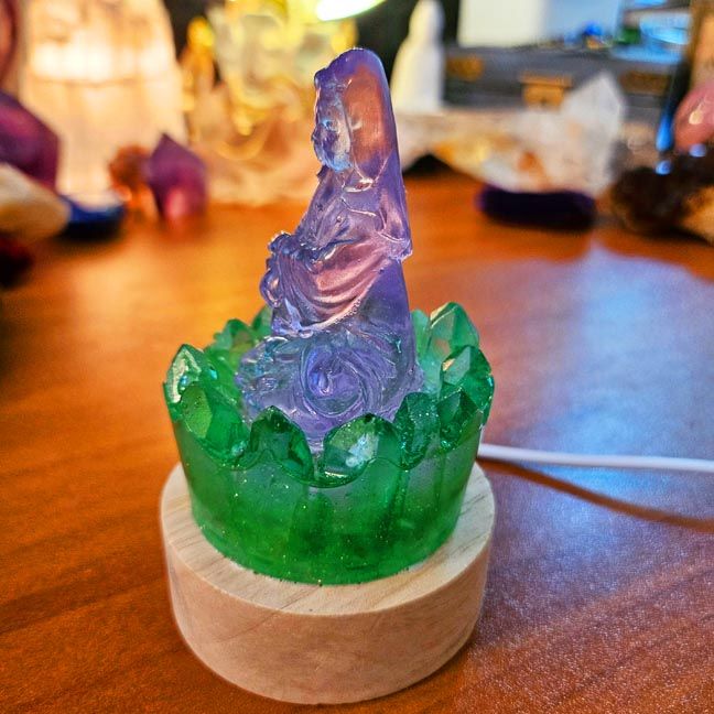 Crystal lamp with a lavender Kuan Yin figurine surrounded by green aura quartz points on a wooden base.