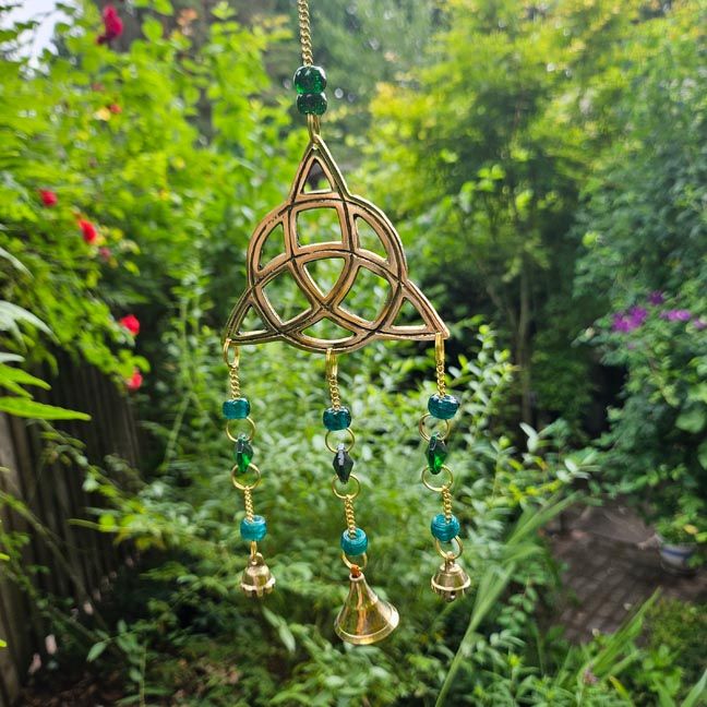 Brass Triquetra wind chime with forest‑green beads, prisms, and bells for unity and protection.