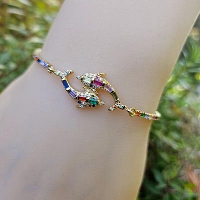 Gold plated rhinestone bracelet with yin‑yang dolphins and adjustable slide clasp.