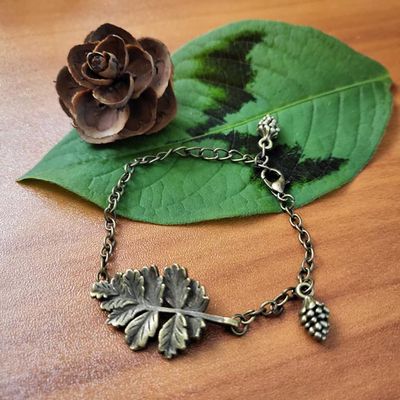 Antique bronze bracelet with a leaf centerpiece and tiny pinecone charms on an adjustable chain.