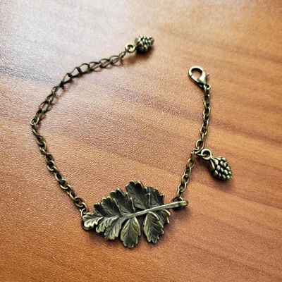 Antique bronze bracelet with a leaf centerpiece and tiny pinecone charms on an adjustable chain.