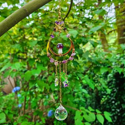 Crescent moon suncatcher with amethyst, mushroom charm, and crystal prism glowing in bright garden light.