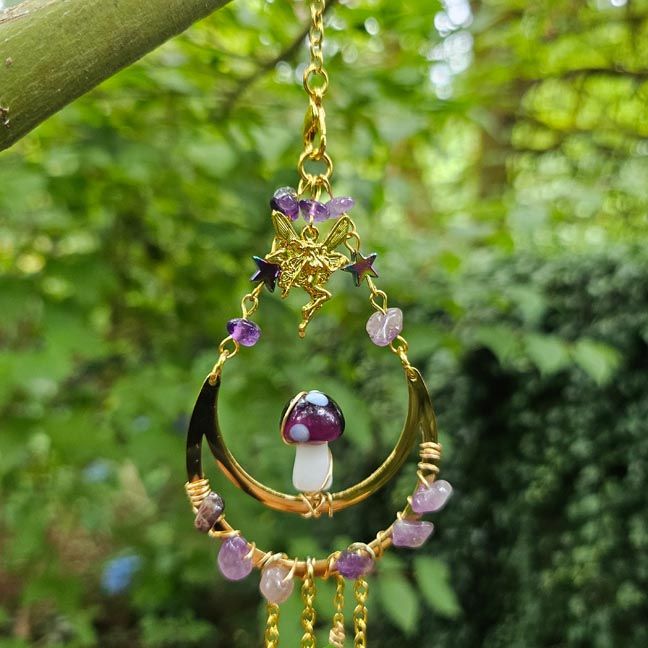 Crescent moon suncatcher with amethyst, mushroom charm, and crystal prism glowing in bright garden light.