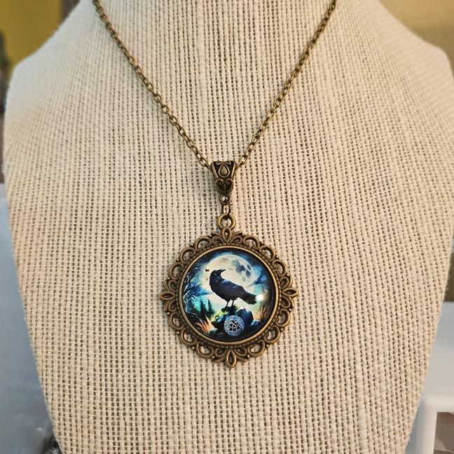 Crow on ancient stone under full moon, iridescent artwork in antique brass pendant with matching pouch.