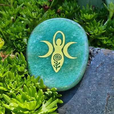 Green Aventurine palm stone with a gold goddess engraving placed among small green plants and rocks