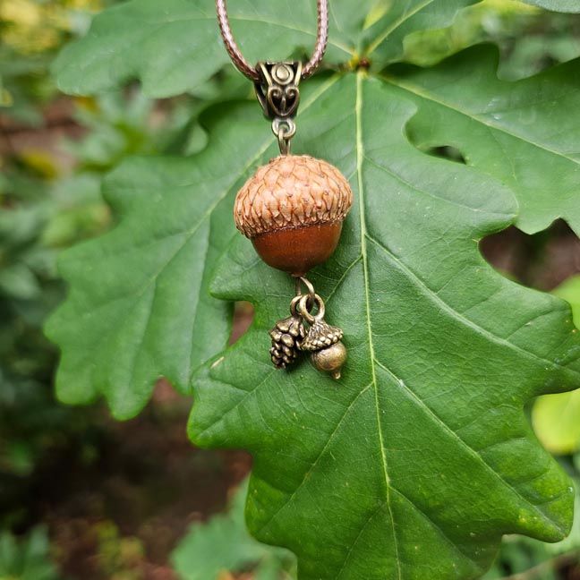 Handcrafted acorn pendant with brass pinecone and acorn charms on a warm brown cord.