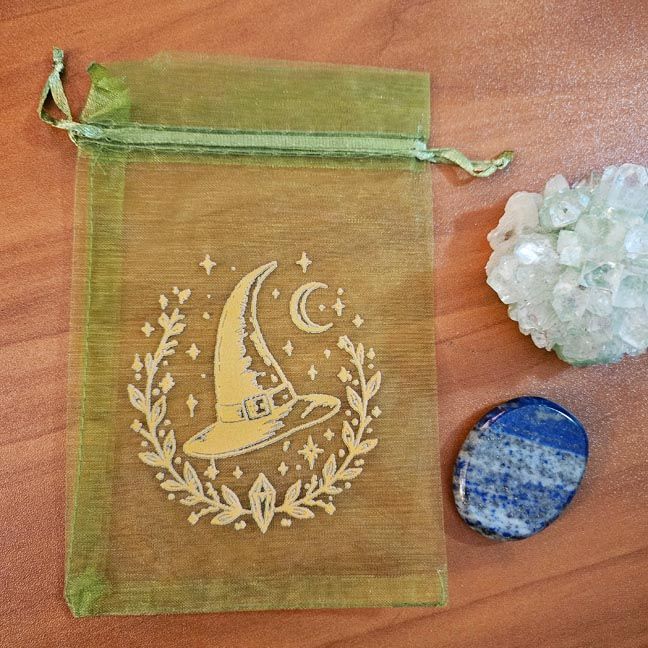 Green organza bag with golden witch hat, moon, and stars printed design.