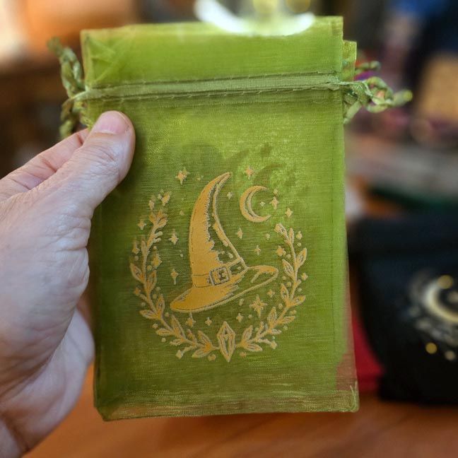 Green organza bag with golden witch hat, moon, and stars printed design.