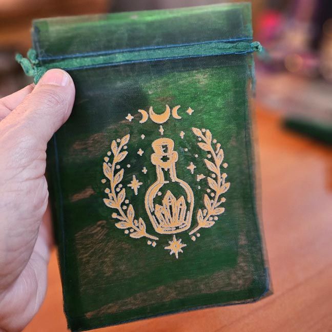 Green organza bag with golden potion bottle surrounded by crystals and celestial motifs.