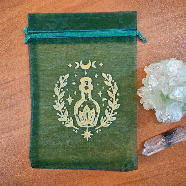 Green organza bag with golden potion bottle surrounded by crystals and celestial motifs.