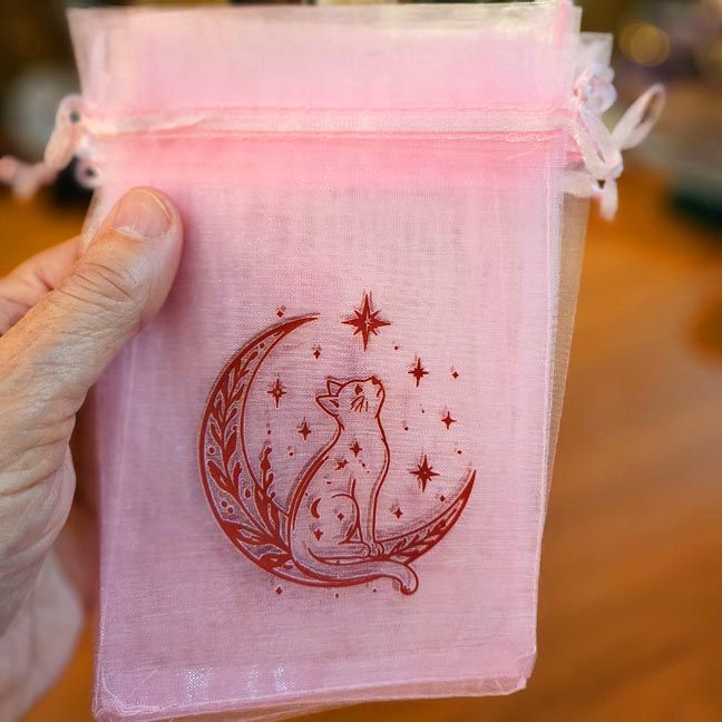 Pink organza bag with cat sitting on crescent moon surrounded by stars.