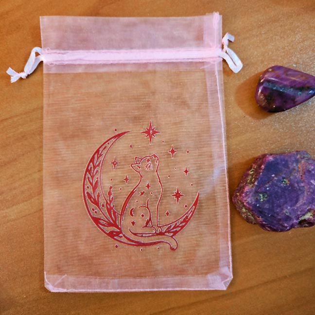 Pink organza bag with cat sitting on crescent moon surrounded by stars.