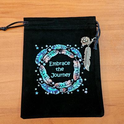 Black velveteen pouch with feather mandala, “Embrace the Journey” text, and silver feather charm.