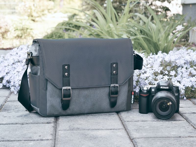 Die graue Foto-Messenger-Tasche steht im Freien auf Gehwegplatten neben einer Spiegelreflexkamera mit Objektiv. 2