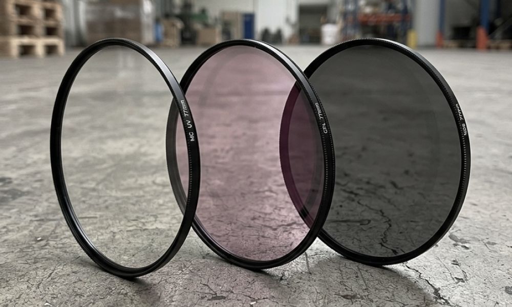 Kamera-Filterset mit einem 77mm MC-UV-Filter, CPL-Polfilter und ND8-Graufilter, aufgestellt auf einem rissigen Betonboden in einer Lagerhalle.