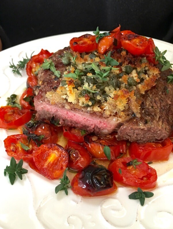 Bistecche alla Sicily -Mesquite wood fired grilled rib-eye steak (locally sourced) topped with a salty crunchy mixture of garlicky capers over a bed of fresh wine broiled tomatoes.