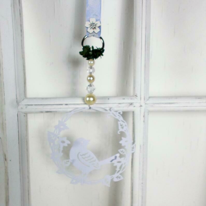 Fensterdeko in weiß aus Metall, mit süßem Vogel und blauem Band