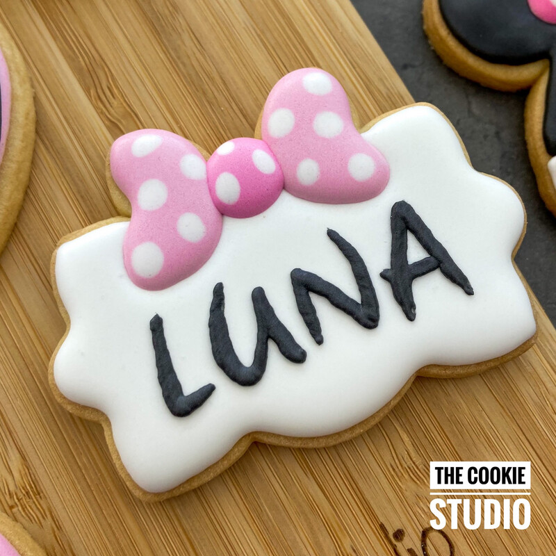 Handgemaakt koekje met roze Minnie Mouse-strik en de naam  – gepersonaliseerd naamkoekje van The Cookie Studio