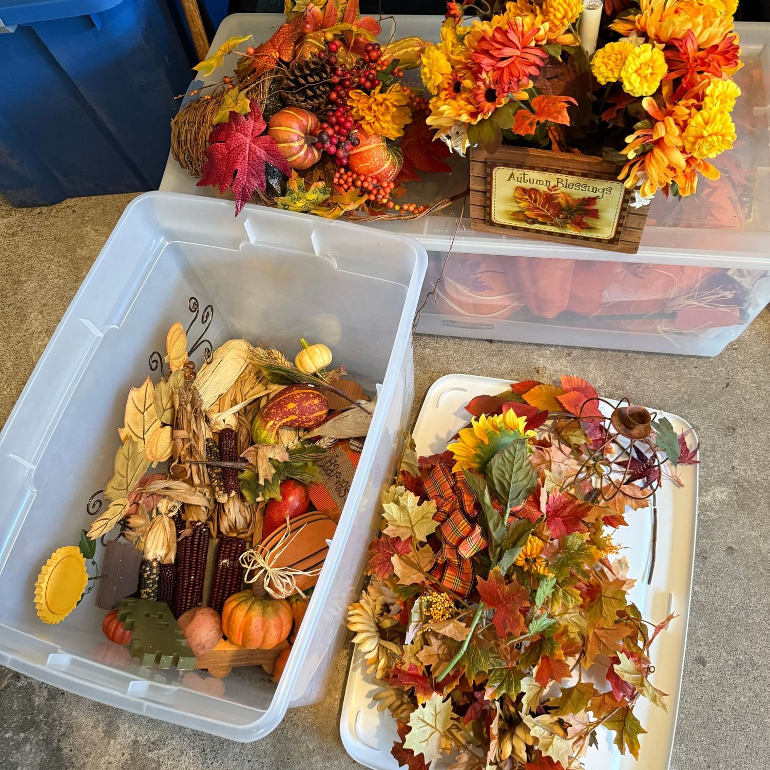 Clear plastic tote with fall garland, corn, small pumpkins, boxed floral arrangement & more