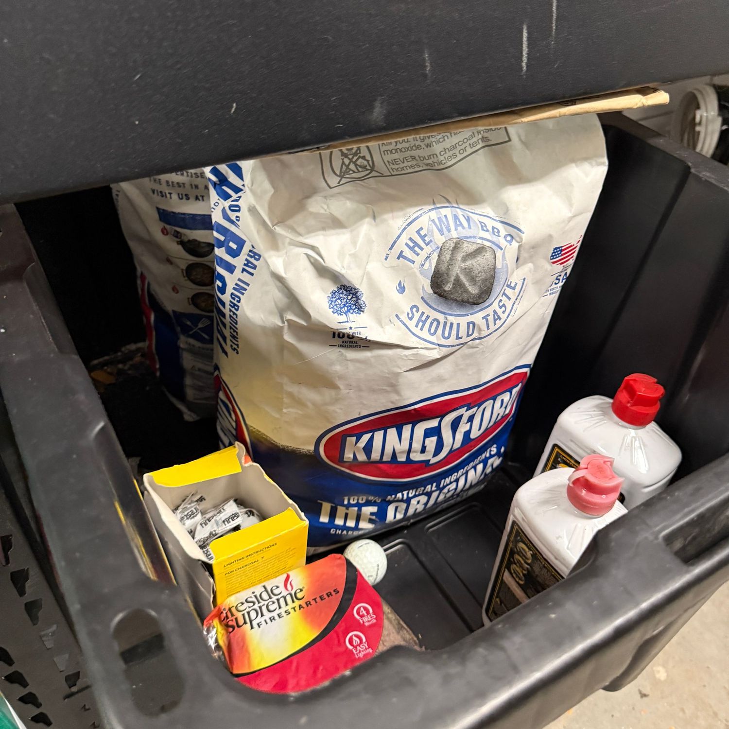 Black bin with two big bags of Kingsford charcoal bricks, semi-full lighter fluid and firestarters
