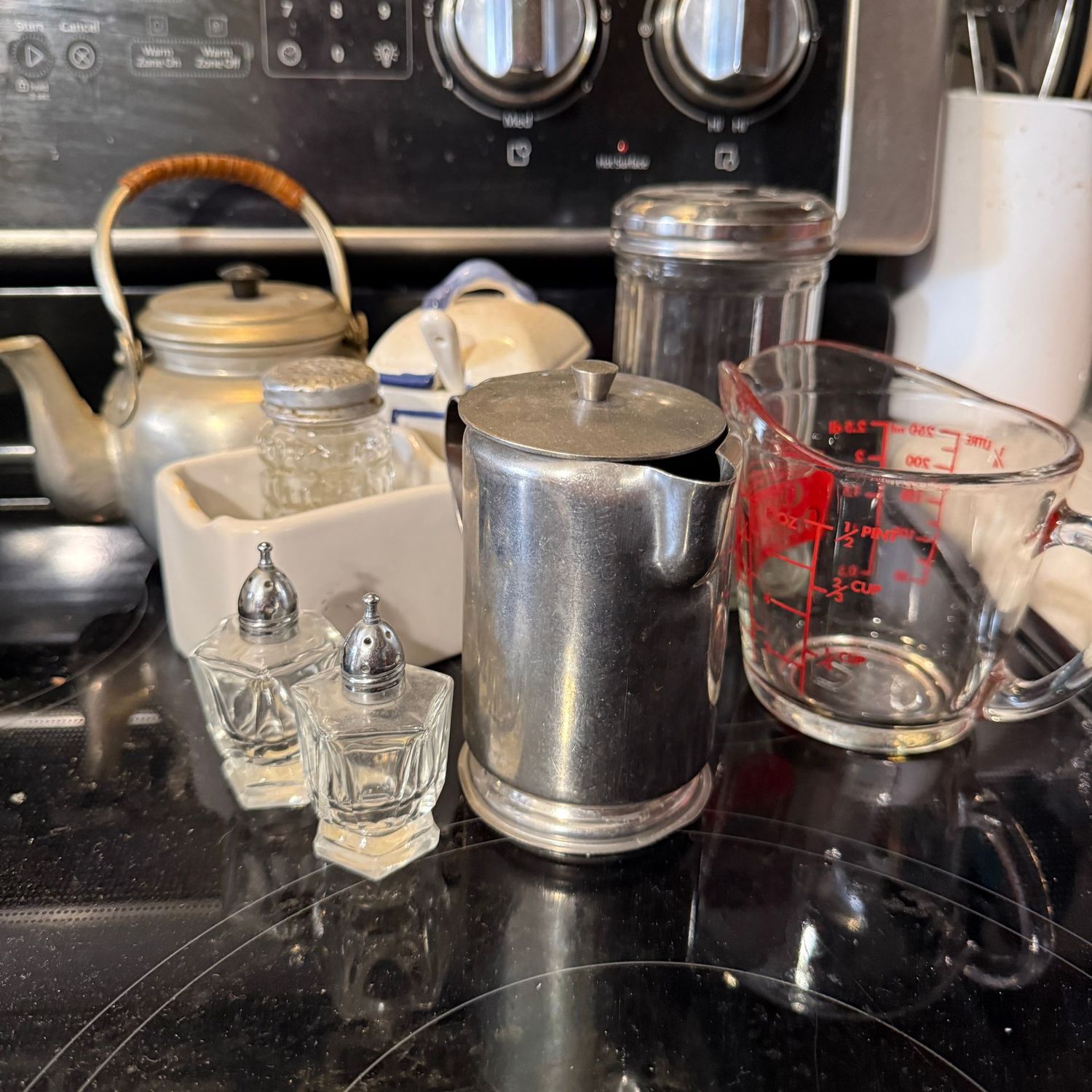 Group of kitchenware with salt, pepper, creamer, measuring cup, sugar shaker, and small metal teapot Group of kitchenware with salt, pepper, creamer, measuring cup, sugar shaker, and small metal teapot
